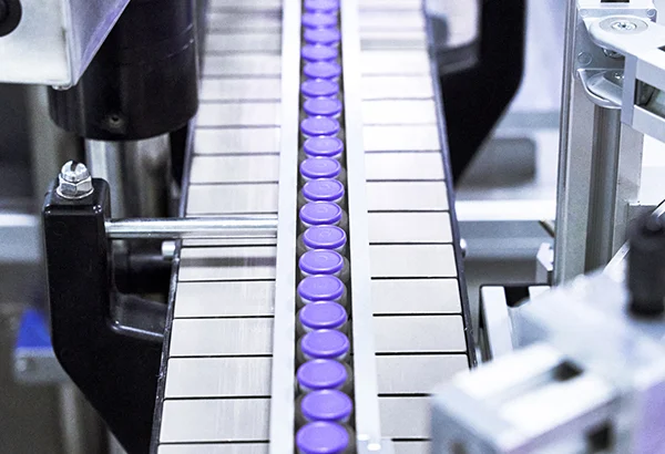 Pharmaceutical vials with purple caps moving along a high-speed conveyor belt in a sterile fill-finish suite.