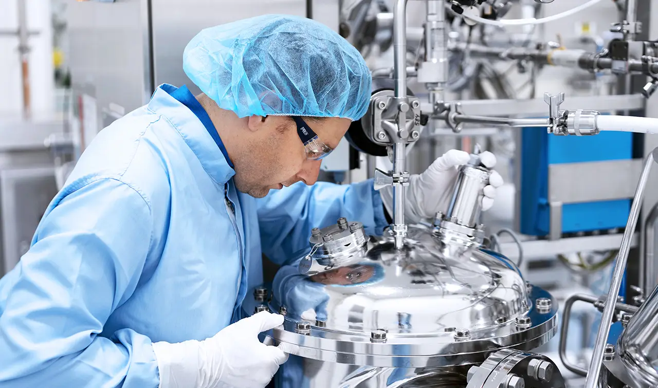 Specialist inspecting a stainless steel solution preparation tank for large-scale biologics and small molecule manufacturing.