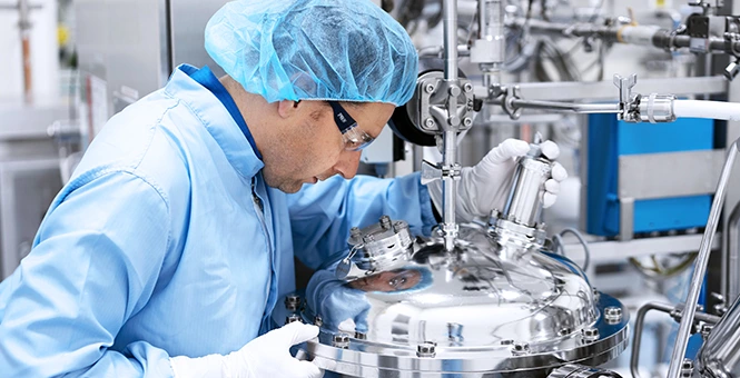 Specialist inspecting a stainless steel solution preparation tank for large-scale biologics and small molecule manufacturing.